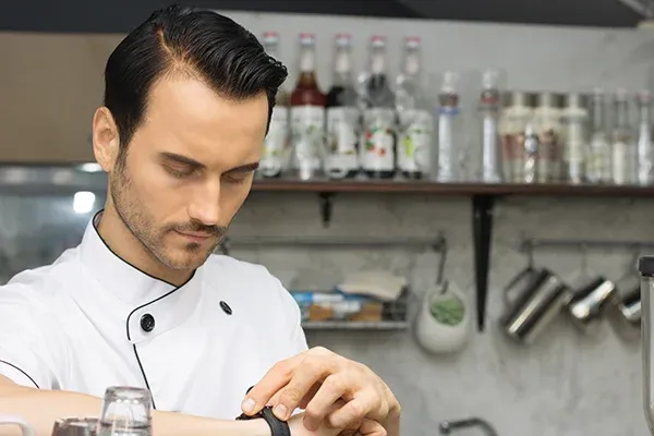 chef en cuisine regardant sa montre dans un restaurant avec des bouteilles en arrière-plan