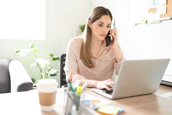 femme au téléphone travaillant sur un ordinateur portable dans un bureau lumineux
