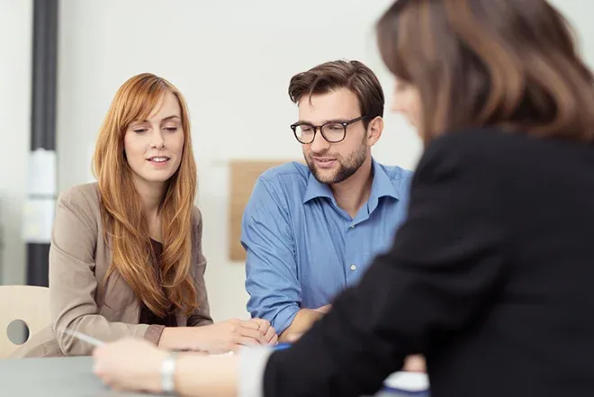 discussion entre trois personnes autour d'une table avec des documents et un ordinateur portable