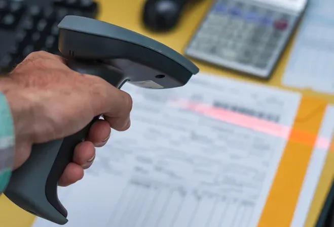 scanner en main sur un bureau avec des documents et une calculatrice en arrière-plan