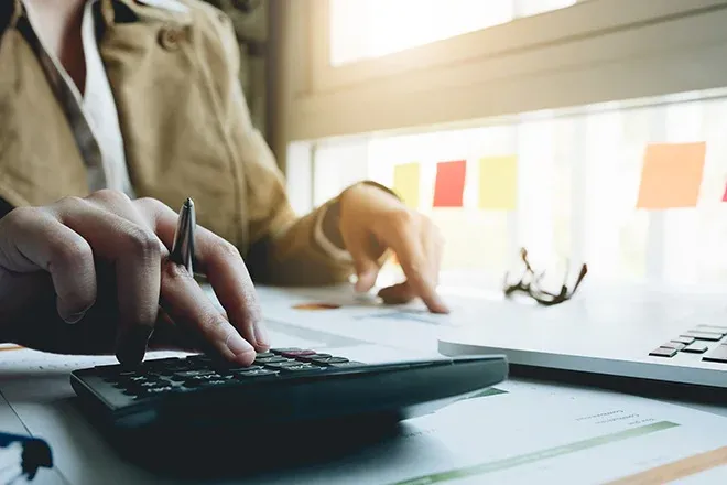 main dans un bureau utilisant une calculatrice avec des notes autocollantes en arrière-plan
