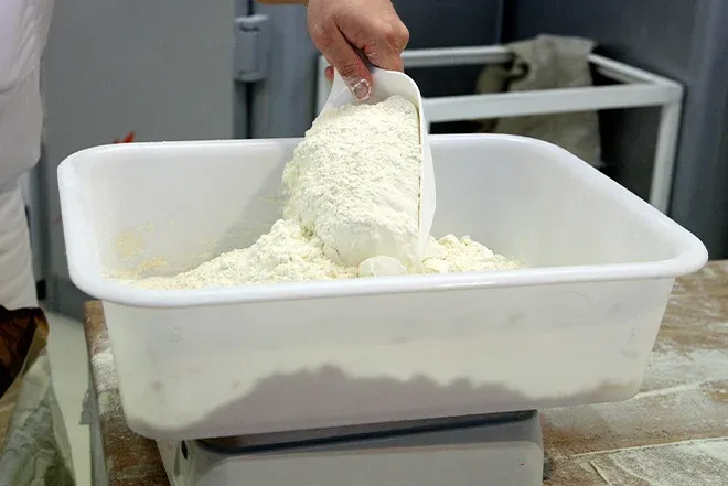 main versant de la farine dans une cuve sur balance de boulangerie