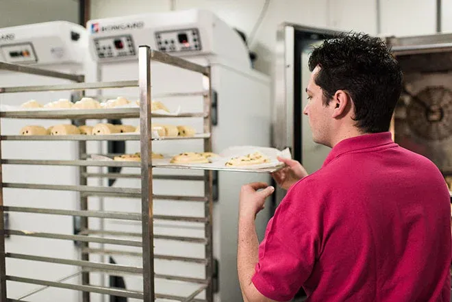 boulanger en train de sortir des pâtes à pain d'un chariot devant des armoires de fermentation