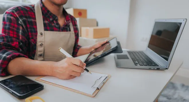 commerçant en tablier saisissant des informations de colis sur tablette et carnet