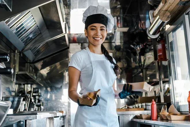 femme souriante en tenue de chef dans un camion de restauration rapide avec des plats à emporter